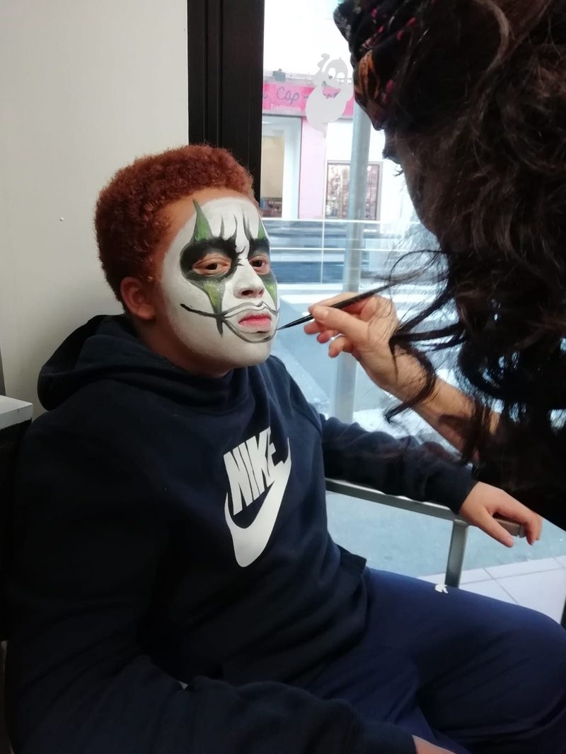 Marine peint un maquillage artistique vert et noir sur le visage d'un enfant lors d'une animation en boutique