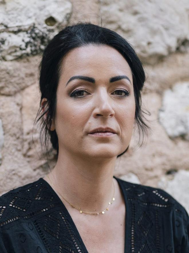 Portrait en extérieur devant un mur de pierre : maquillage sobre, teint unifié sans effet de masque, regard souligné de brun