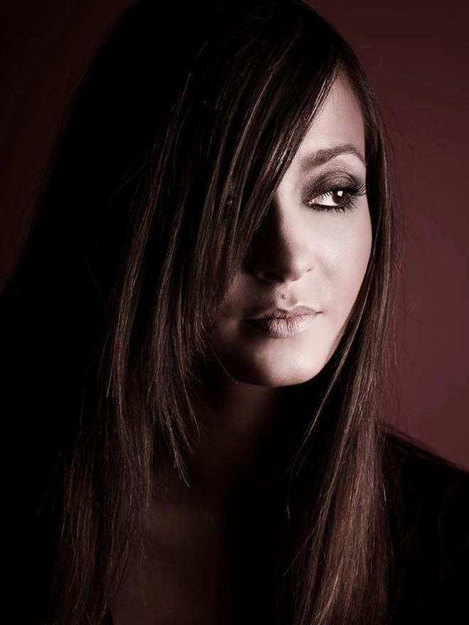 Portrait en clair-obscur sur fond prune, cheveux longs devant l’épaule, regard charbonneux et bouche nude, maquillage pensé pour une lumière basse