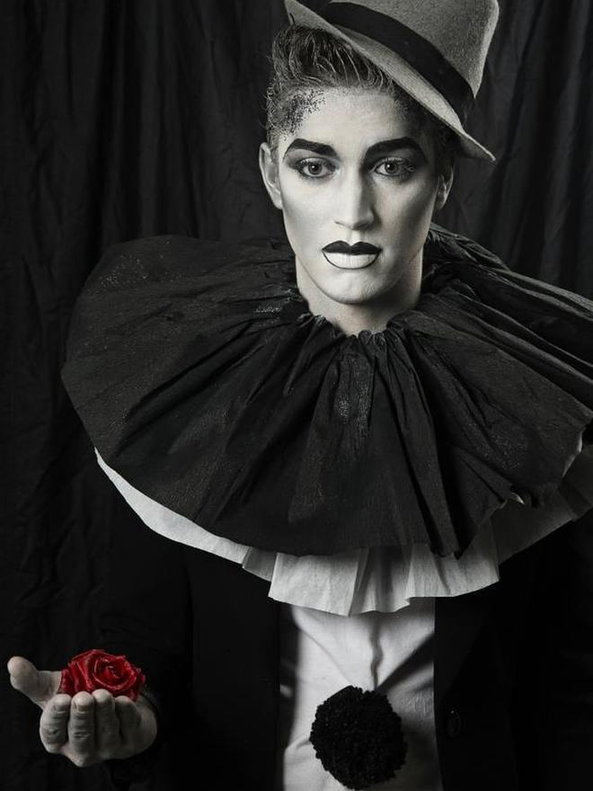 Maquillage de scène en noir et blanc : visage poudré blanc, lèvres et sourcils marqués, collerette plissée et chapeau melon, une rose dans la main
